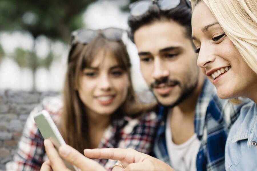 Zwei Frauen und ein Mann schauen zusammen auf ein Smartphone.