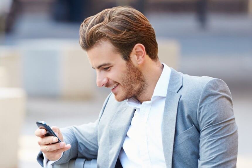 Ein Mann (Mitte 30) sitzt auf einem Sessel und tippt Inhalte in sein Smartphone ein.